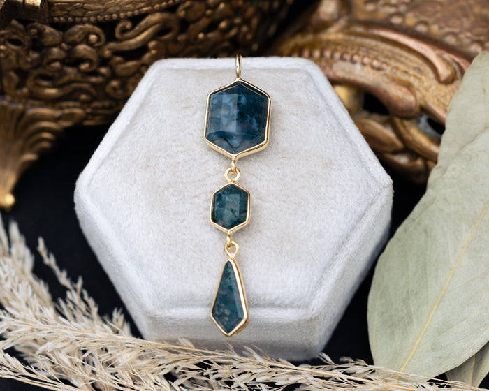 Moss agate pendant on a hexagon cushion with decorative elements in the background