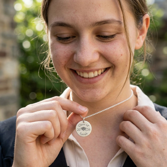Graduate holding a silver engraved graduation necklace, personalized with class year and custom name.
