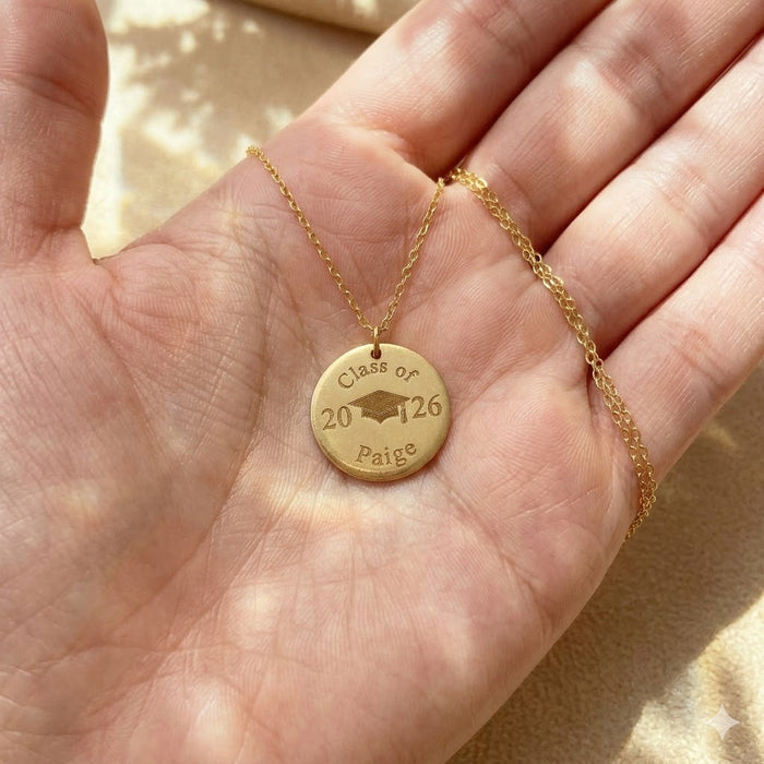 Close-up of gold personalized graduation necklace held in hand, engraved with Class of 2026 and graduate name Peyton.