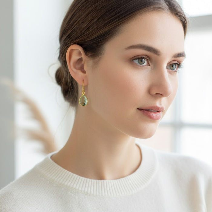 Close-up of woman wearing green amethyst dangle earrings with faceted teardrop gemstone, elegant gold drop earrings for everyday or special occasions.