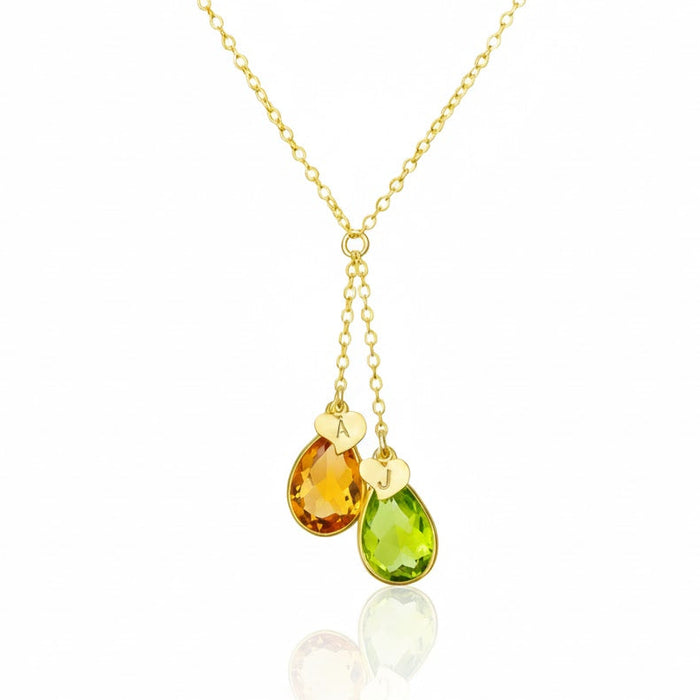Dainty initial birthstone lariat style necklace with two faceted teardrop charms hanging from a delicate gold chain, featuring personalized heart initial discs above each gemstone. Shown in warm citrine and bright peridot to represent family or couple birthstones, this customizable necklace is perfect as a mom necklace, couples gift or best friend jewelry, and a meaningful personalized birthstone necklace for everyday wear or special occasions.