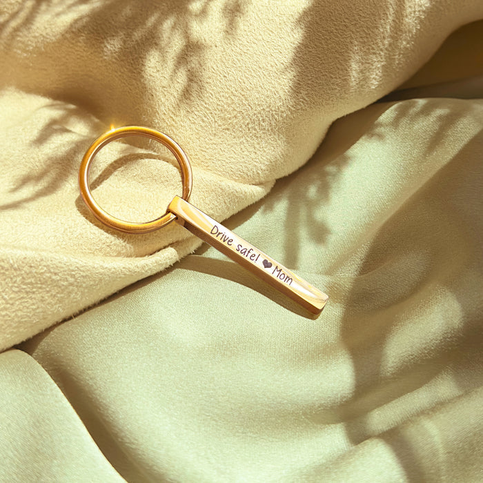 A gold mini 3D bar keychain resting on soft green fabric emphasizes the elegant, dainty keychain scale and polished edges. Crisp laser engraving along the side demonstrates readability on the smaller bar, while the spring key ring remains sturdy for daily use. Personalize this custom bar keychain with names, roman numerals, or GPS coordinates for anniversaries, travel mementos, or groomsmen sets.