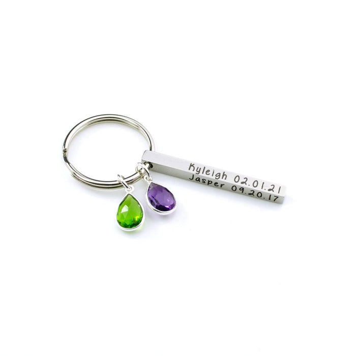 Clean studio image showing a silver kids name keychain with a slim engraved bar and two vibrant birthstone drops. The modern spring ring keeps the profile sleek while the compact 40×4 mm bar supports names, initials, or date keychain engraving on multiple sides. A sweet, minimalist way to celebrate children or grandchildren for Mother’s Day or birthdays.