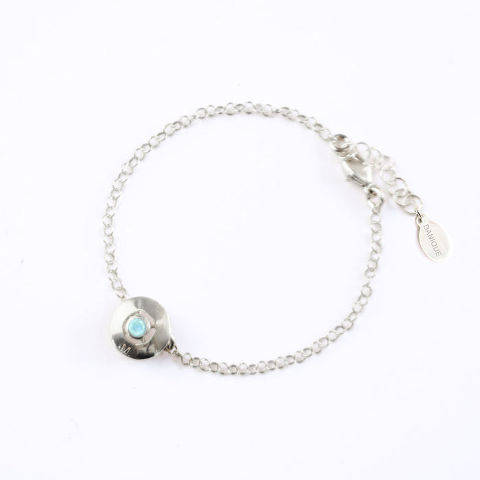 A 925 sterling silver donut bracelet with an aqua chalcedony stone and the letter "M" engraved on the bottom of the disc rests against a white background. This bracelet is hypoallergenic and is sure to make the day of anyone who receives this as a gift! This is the perfect thing for Mother's Day!