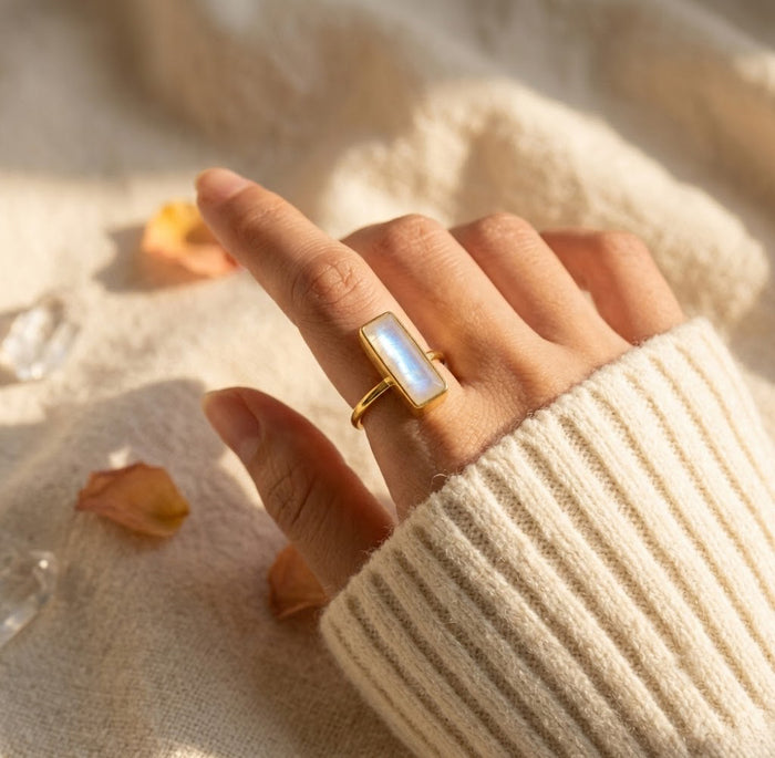Moonstone bar ring worn on a hand with a cream sweater, showing the rectangular June birthstone ring in warm gold.