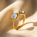 Adjustable moonstone triangle ring in gold with two 8mm June birthstone stones on warm fabric.