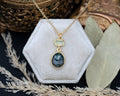 Gold necklace with moss agate & prasiolite pendant on a hexagonal white velvet stand with decorative elements.