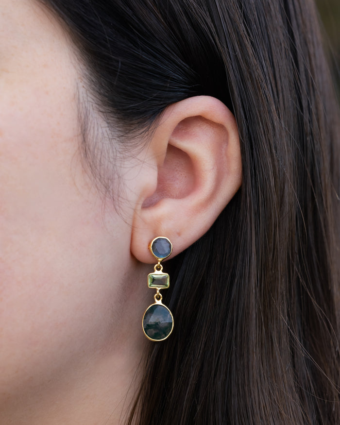 Close-up of an ear wearing a gold earring with gemstones.
