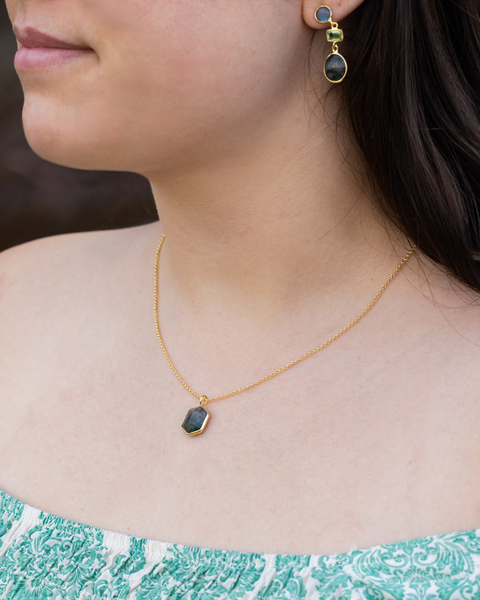 Close-up of a person wearing a gold necklace and earrings with moss agate.