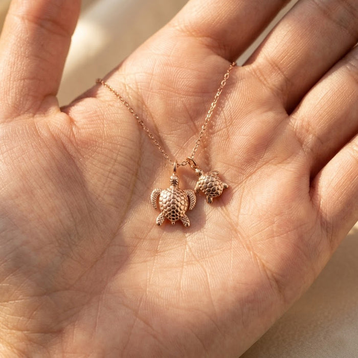Mama turtle and baby turtle necklace held in hand, shown in rose gold finish as a meaningful gift for mothers and daughters.