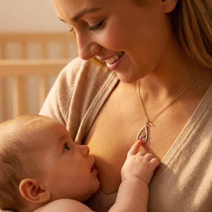 Mother wearing personalized birthstone necklace while holding baby, a meaningful custom jewelry gift for new moms.