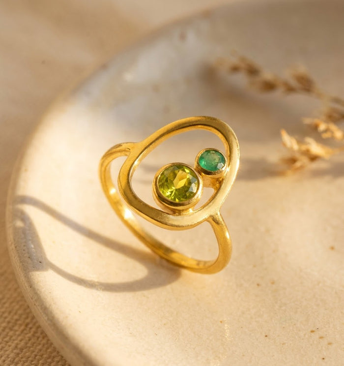 Mother and child birthstone ring in gold with one larger green mom stone and one tiny child stone in an open oval setting.