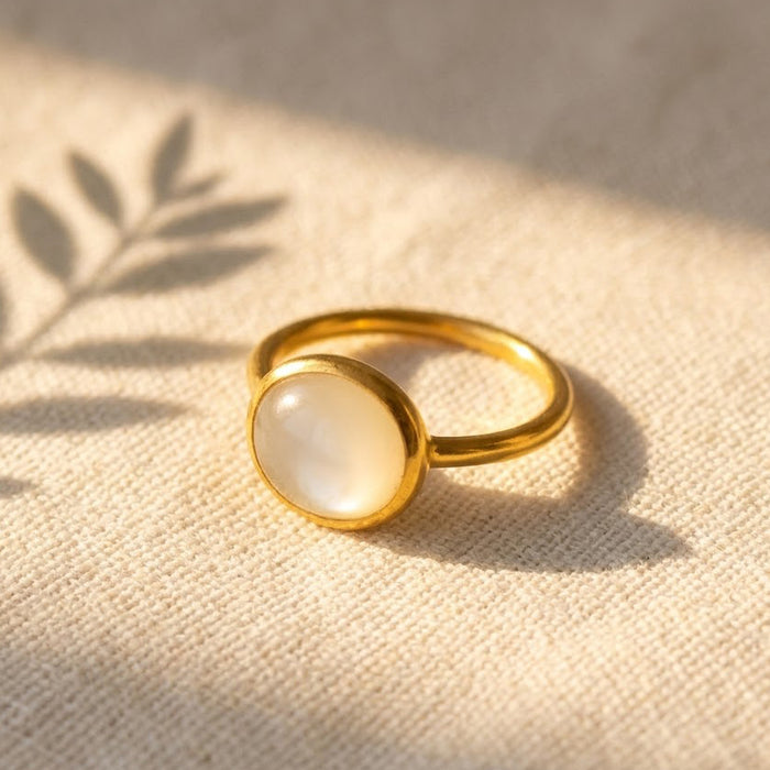 Oval mother of pearl cabochon ring in yellow gold vermeil on a soft neutral background with warm natural light.