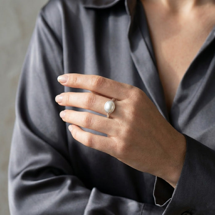Oval mother of pearl ring worn on hand with a dark blouse, styled as an elegant gemstone ring for everyday wear.