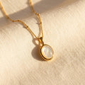 Mother of Pearl oval pendant necklace in gold shown on soft cream fabric in natural sunlight.