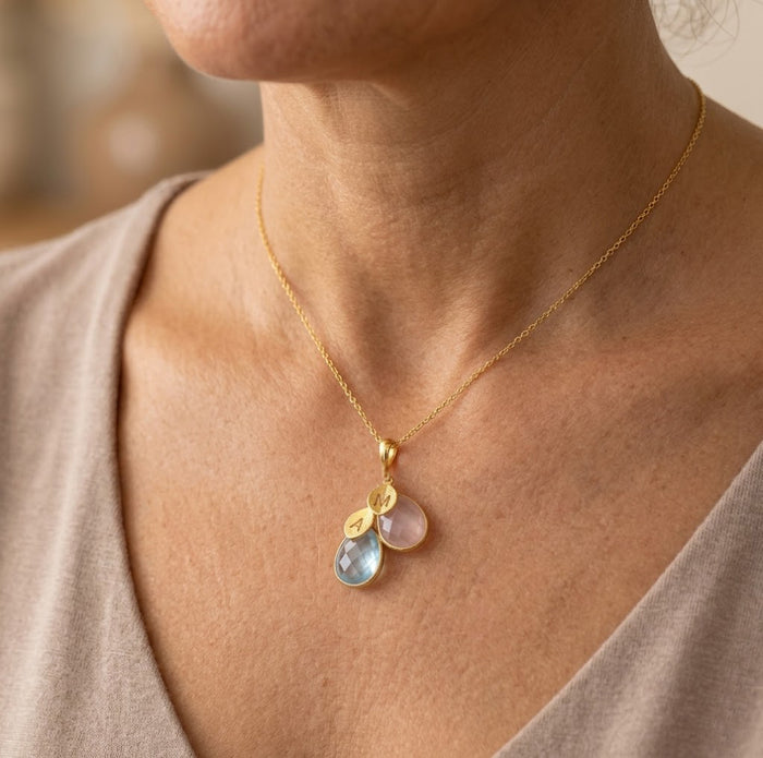 Model wearing custom family birthstone necklace, a delicate personalized mom necklace with cascading gemstone charms and initials.