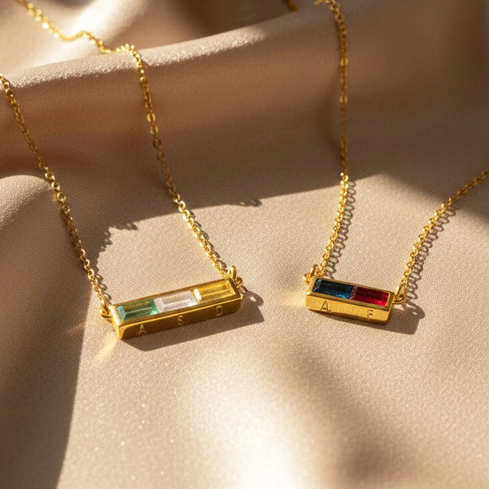 Personalized birthstone bar necklaces in gold with rectangular gemstones on soft fabric.