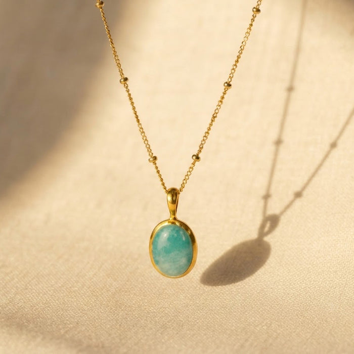 Natural amazonite oval bezel necklace in gold shown in warm sunlight on textured fabric.