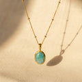 Natural amazonite oval bezel necklace in gold shown in warm sunlight on textured fabric.