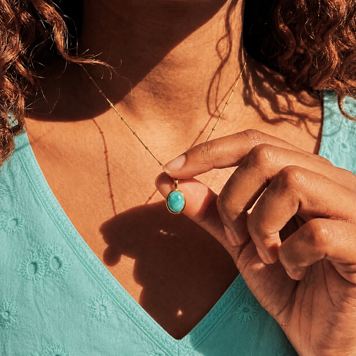 Model wearing an amazonite oval gemstone necklace with aqua clothing in golden sunlight.