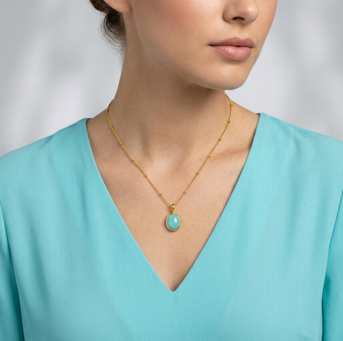Model wearing a dainty amazonite oval bezel necklace with an aqua V-neck top.