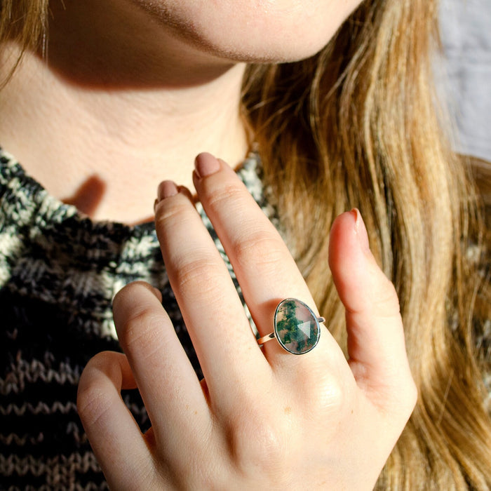 Woman wearing a large green moss agate gemstone ring with natural forest-like inclusions in warm sunlight