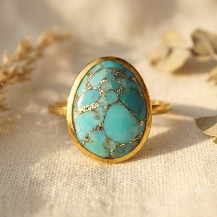 Oval natural turquoise ring with copper veining in a polished yellow gold vermeil bezel on a neutral cream background.