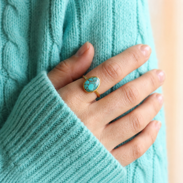 Woman wearing an oval turquoise statement ring with an aqua knit sweater, showing the ring’s scale and vivid blue color.