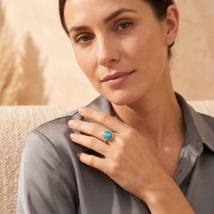 Woman wearing an oval turquoise ring with a gray blouse, showing the bold gemstone size and elegant everyday styling.
