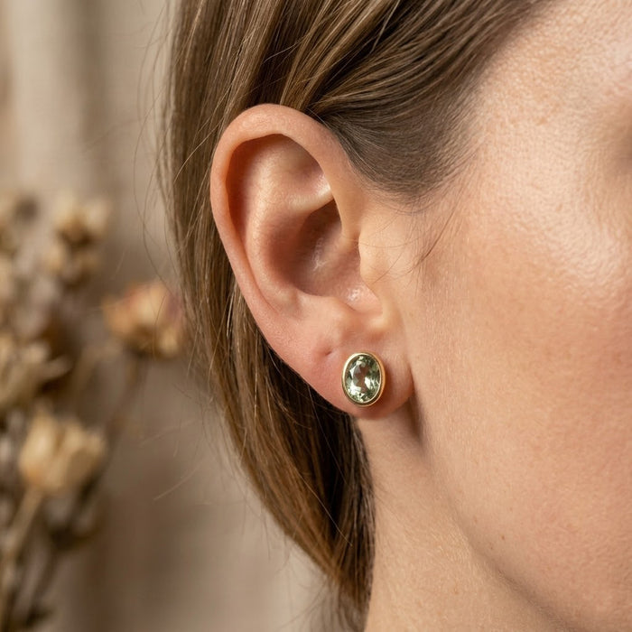 Model wearing green amethyst oval stud earrings, showing the bezel set gemstone earrings on the ear.