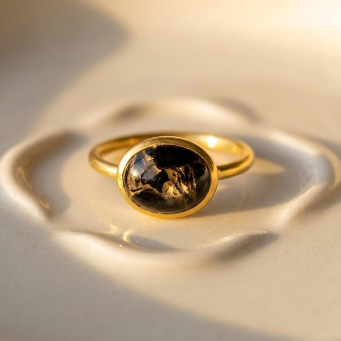 Oval black obsidian cabochon ring in yellow gold shown on warm beige background