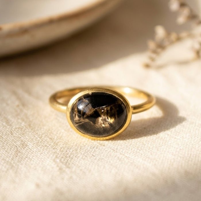 Oval black obsidian cabochon ring in gold setting on beige fabric with soft natural light