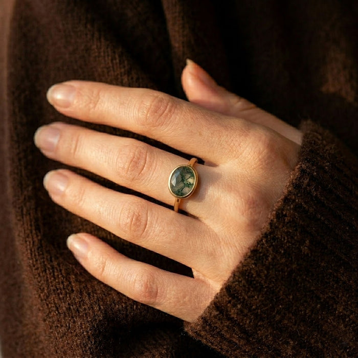 Moss agate ring worn on hand with a dark sweater, showing the oval green stone size and natural everyday styling.