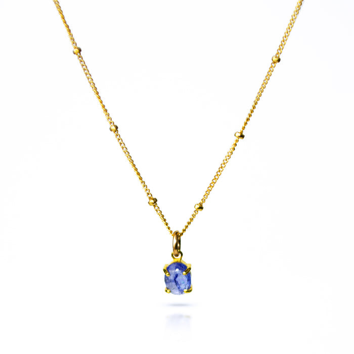 Oval natural tanzanite Cabochon Bezel Set into a 925 Sterling Silver Pendant Plated in 18k Vermeil Gold sitting on a 14K Gold Filled Cable Chain resting on a white background. Great as a gift for fall lovers and sophisticated blue color and sunstone lovers.