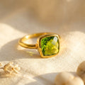 Cushion cut peridot ring in gold bezel setting with bright green gemstone