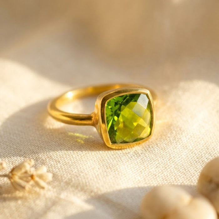 Cushion cut peridot ring in gold bezel setting with bright green gemstone