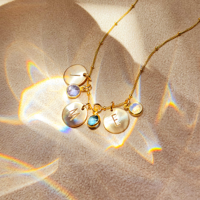 Personalized gold disc birthstone charm necklace with engraved initial letter pendants and bezel-set gemstone charms on a delicate beaded chain, custom family name jewelry for mom or grandma, meaningful birthday or Mother’s Day gift idea.
