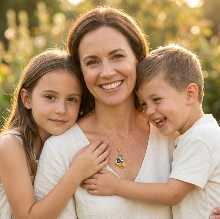 Mother wearing a custom birthstone and name necklace with her children, personalized family jewelry designed to represent kids or grandkids.