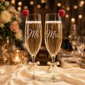 Personalized Mr and Mrs champagne flutes with frosted engraving, raspberries, gold bows, ivory satin fabric, and warm wedding lights.