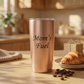 Personalized copper coffee tumbler engraved with “Mom’s Fuel,” styled with coffee beans and a croissant as a custom coffee lover gift for mom.