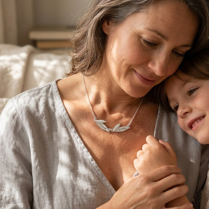 Mother wearing a personalized leaf name necklace while holding her child, a sentimental family necklace customized with kids’ names.