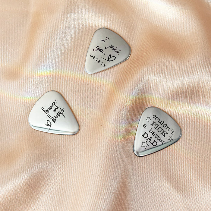 Three engraved guitar picks displayed on fabric, showcasing custom text and handwriting options, perfect as personalized musician gifts, bulk orders, or engraved keepsakes.