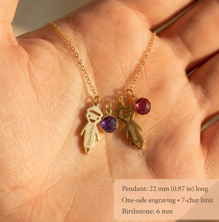 Close-up of engraved boy and girl child charms with colorful birthstones shown in a hand for scale.