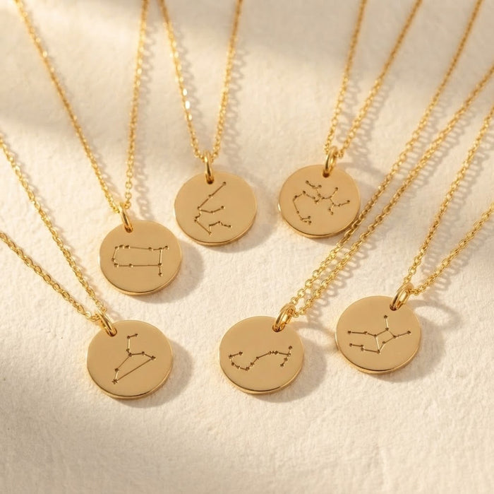 Collection of personalized zodiac constellation necklaces with round engraved disc pendants in warm natural light.