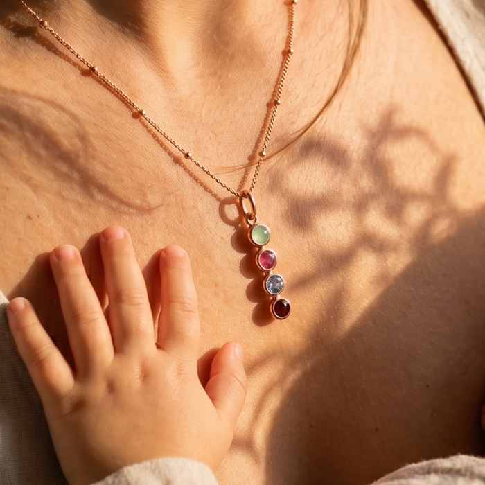 Necklace with colorful birthstones to represent family worn by a mother, with a child's hand touching it.