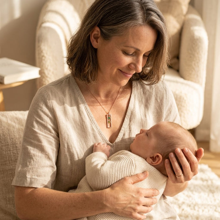 New mom wearing a vertical birthstone necklace while holding her baby, meaningful personalized jewelry gift for mothers.
