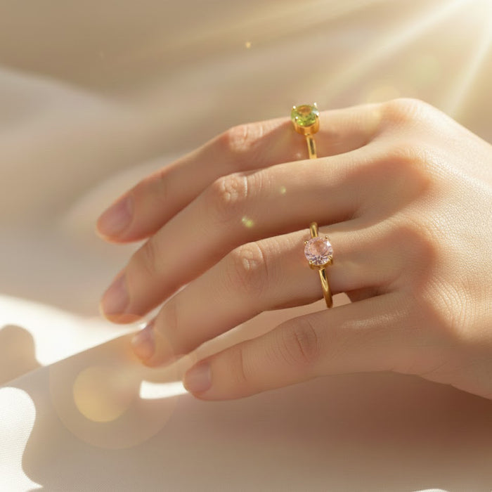delicate hand wearing two dainty stackable birthstone rings in 18K gold vermeil over .925 sterling silver, one set with a light green peridot-style stone and the other with a soft blush pink gemstone, minimalist round solitaire bands perfect for layering as a personalized mothers ring, promise ring or everyday birthstone jewelry gift for birthdays, anniversaries, or Mother’s Day