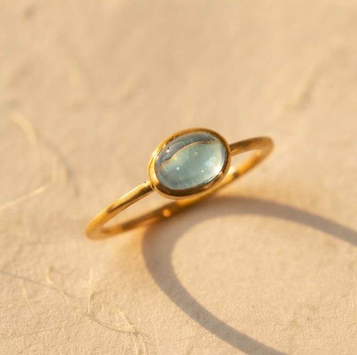 December blue topaz oval cabochon gemstone ring in a yellow gold bezel setting