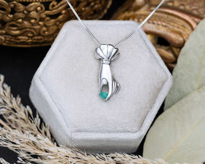 Silver hand pendant with a raw emerald in a hexagonal jewelry box.