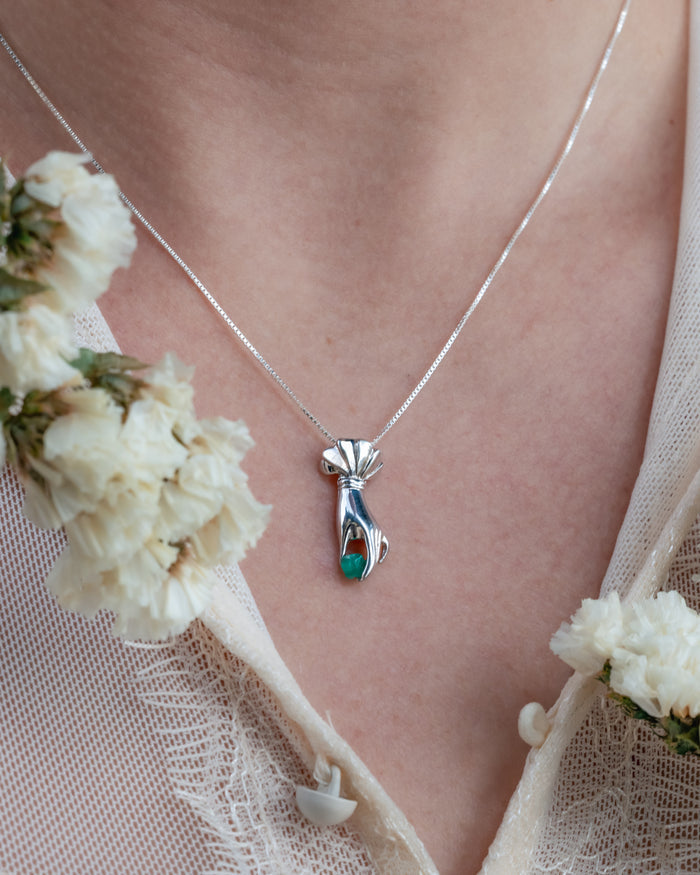 Necklace with a hand pendant worn by a person, surrounded by white flowers.